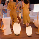 People socializing on a wooden deck with illuminated stools and standing lamps.