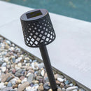 Black lattice-patterned solar light on a garden spike on a pebble ground with water in the background