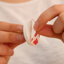 Person holding a small white container with red text, against a neutral background.