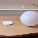 Umage Orbit Portable Table Lamp on a table next to its charging mat. The Umage Portable Light has a handle to carry it