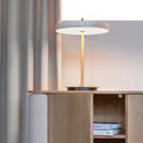 Umage Asteria Table Lamp casting a glow of light over a sideboard which is open with books in.