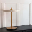 Umage Asteria Table Lamp with Brass basse on a black sideboard infront of white panelled walls