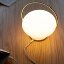 Umage Orbit Portable Table Lamp shining bright on a table charging wirelessly on a usb charging base