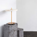 Umage asteria in pearl White looking modern and sleek in a white room with a black floor. The table lamp is pictured placed on grey blocks as a table.