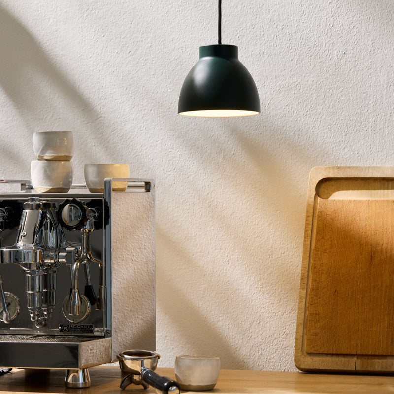 Espresso machine on a wooden counter with a light-colored wall and pendant light.