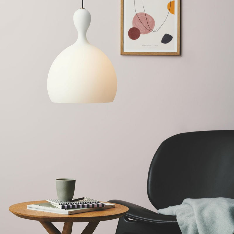Modern interior with a glass pendant light, side table, and armchair against a light pink wall.
