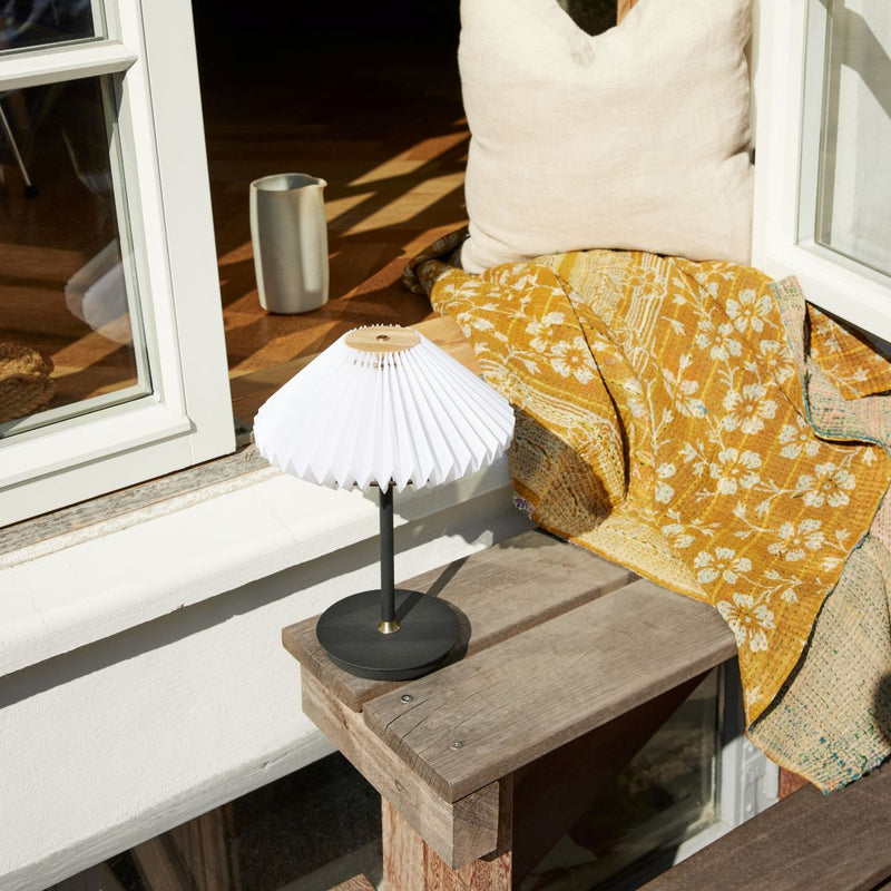 Small white lamp on a wooden surface next to a yellow patterned blanket by a window.