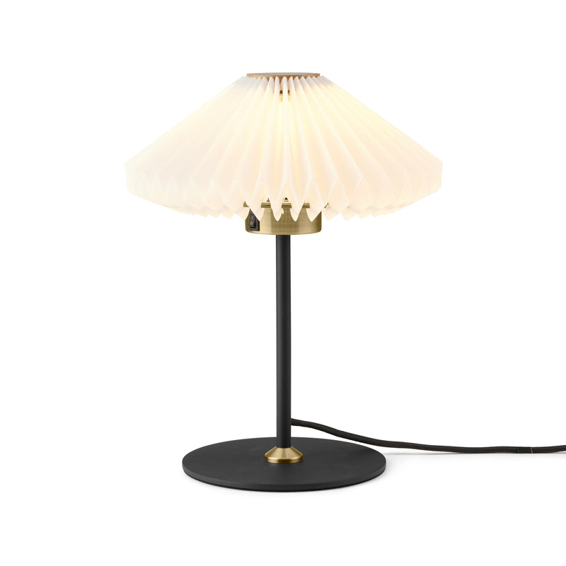 Table lamp with a black base, gold accents, and white pleated shade on a white background