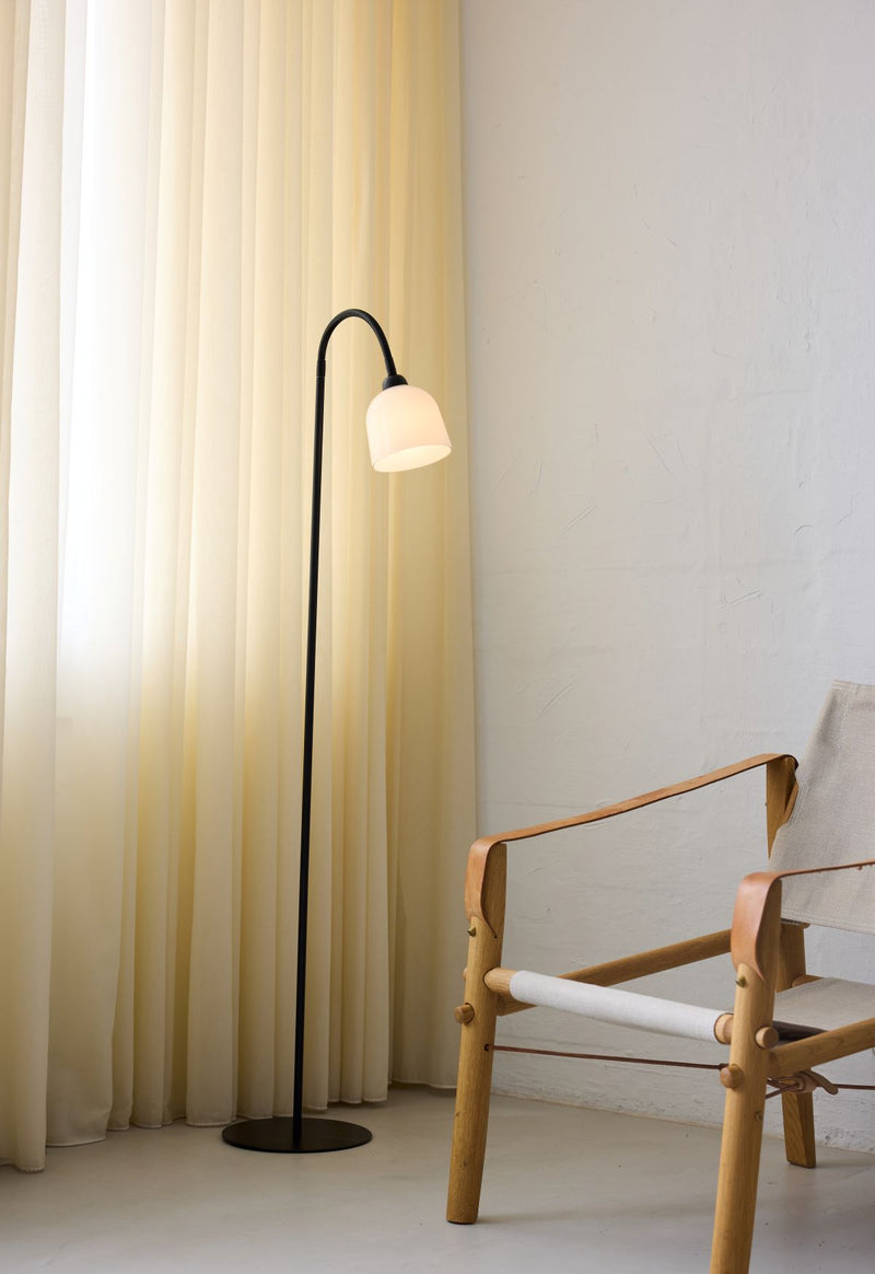 Floor lamp with a light bulb next to a wooden chair against a white wall.