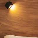 Black wall-mounted light fixture on a wooden wall with a soft glow.