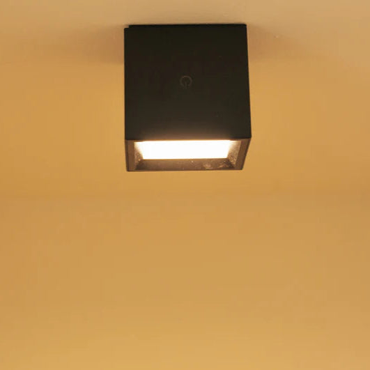 Square ceiling light fixture on a beige wall with a textured baseboard.