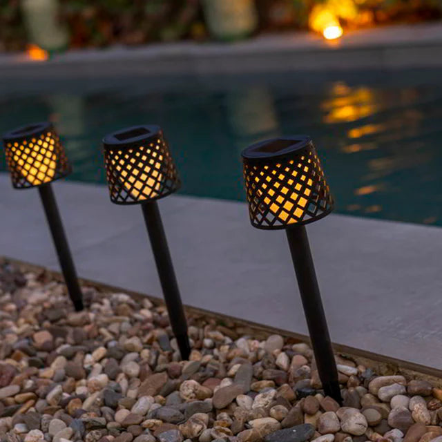 Three solar-powered garden lights on pebbles near a pool at night.