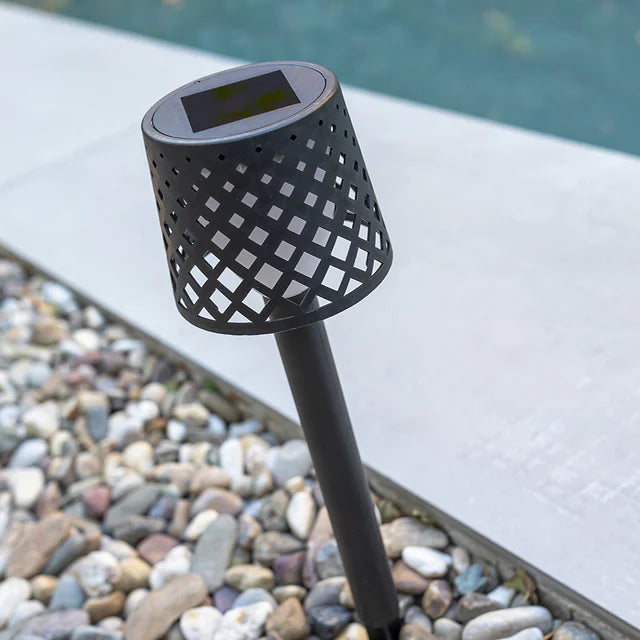 Black lattice-patterned solar lamp on a pebble ground with water in the background