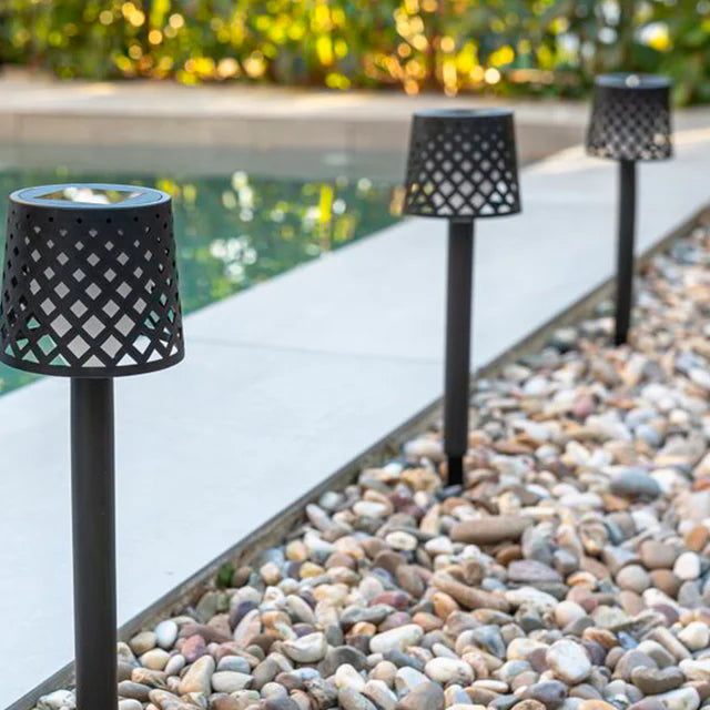 Black lattice-patterned outdoor lamps along a pebble-lined pool area.