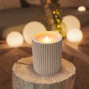 Candle in a textured holder on a wooden block with blurred lights in the background