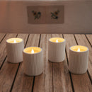 Four ribbed candle holders with lit candles on a wooden surface.