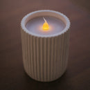 Candle in a ribbed container with a soft glow on a dark background