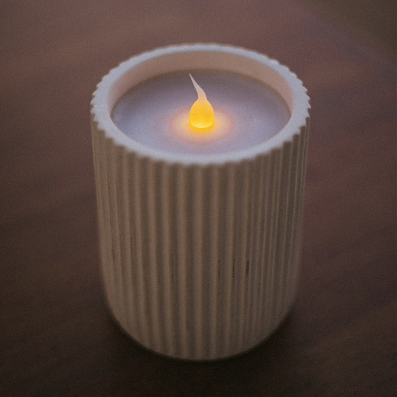 Candle in a ribbed container with a soft glow on a dark background