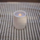Candle in a textured holder on a striped fabric surface