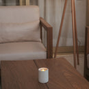 Candle on a wooden table with a blurred chair and lamp in the background