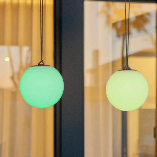 Two green spherical pendant lights hanging above a table with plants in an indoor setting.
