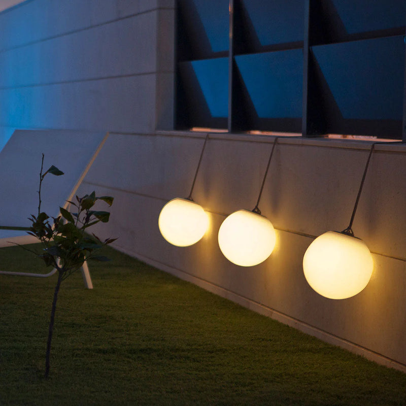 Three spherical outdoor lights hanging against a modern building facade at night.