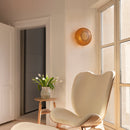 A relaxing room with a comfortable chair, side table with flowers and a Clava Wall Light by umage casting warm light patterns on the walls