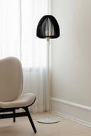 Clava Wooden Lampshade in black oak on a floor lamp next to a chair