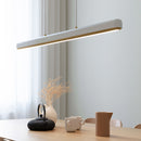 Umage Hazel Branch Pendant Light. A modern pendant light with a built-in LED panel, featuring a soft white diffuser and brass details. The light is hanging over a dining table in a room with a light interior.