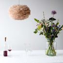 Umage EOS pink lampshade on a cieling lighting in a white room with a white table. on the table is a vase of flowers and bottle of wine.