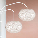 A Pair of Delicate Feather Lampshades by Umage hang together against a soft pink wall casting a soft light