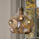 A contemporary Hand Blown amber-coloured glass pendant light hanging near a window, with visible light patterns inside the glass.