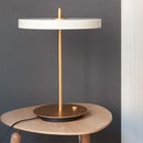 White Umage Lamp, Asteria Table Lamp on a small wood side table against a grey wall.