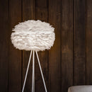 Umage Medium feather lampshade on a floor lamp  against a dark wood clad wall.