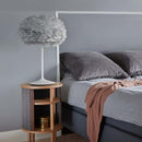 A grey bedroom with rey Bed linen and walls, a wooden sidetable with a lamp with a EOS feather Lampshade by Umage in Light Grey